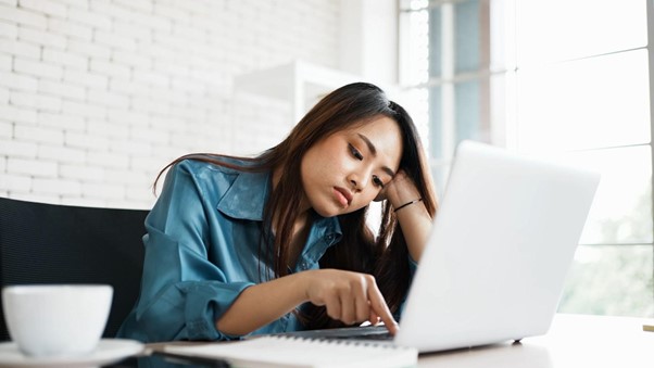 Vrouw kijkt verveeld naar haar laptopscherm tijdens het werken
